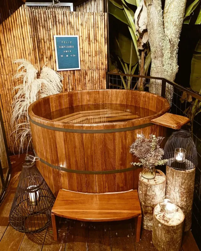 Bañera al aire libre en glamping con madera natural, velas y decoración cálida, ideal para una experiencia romántica