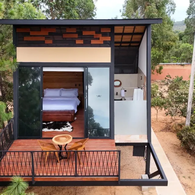Cabaña moderna con terraza y ventanales, rodeada de árboles, experiencia de glamping moderno para parejas.